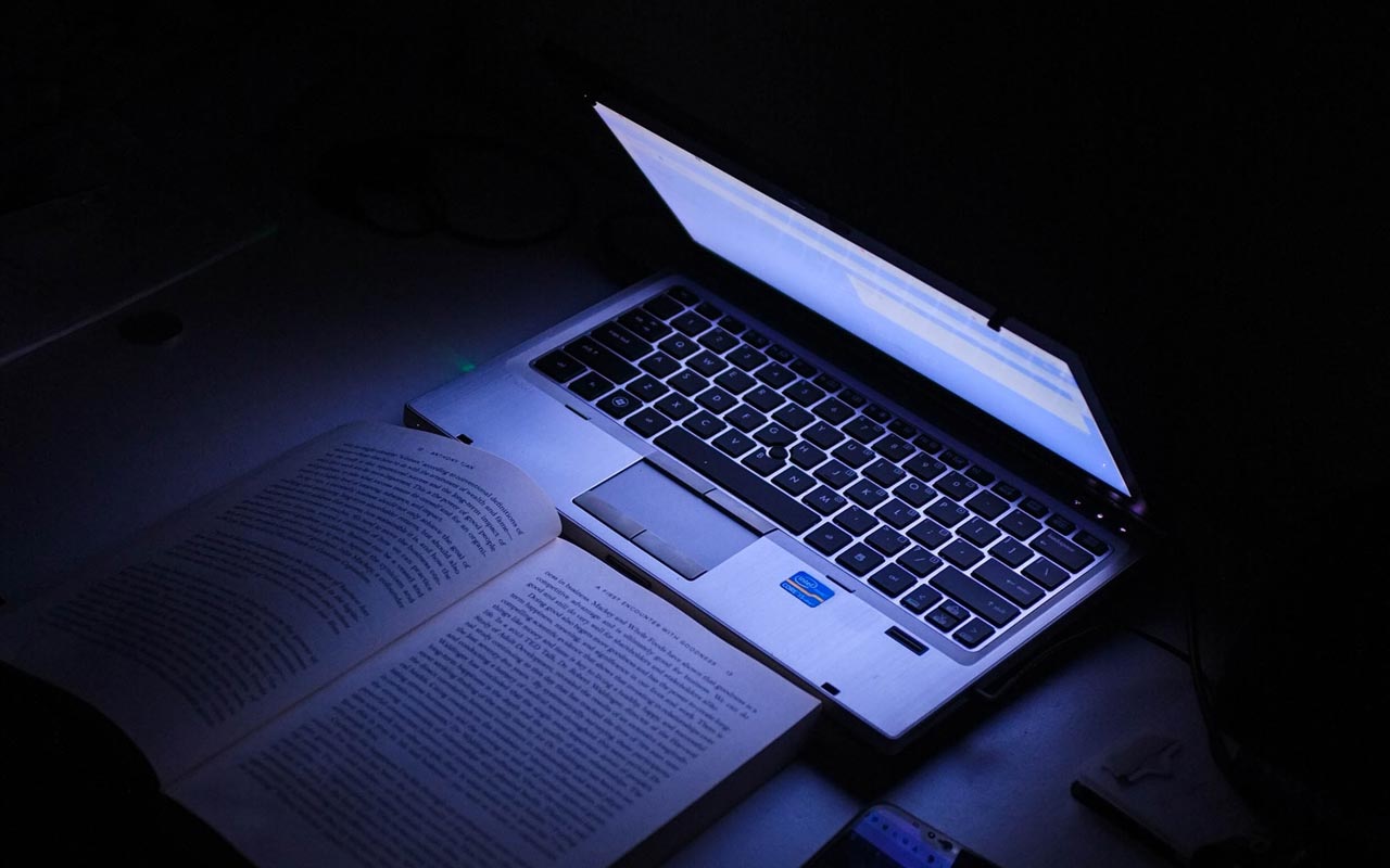 笔记本电脑在黑暗的房间里照亮一本书。