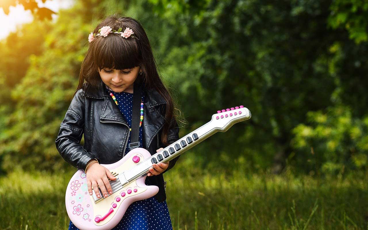 一个穿着皮夹克，头发上插着鲜花的女孩在弹一把粉红色的塑料吉他。