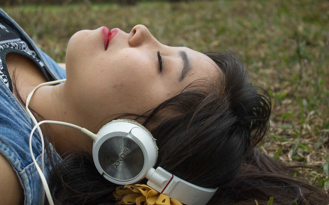 一个戴着大耳机的女人闭着眼睛躺在草地上，专注于音乐。