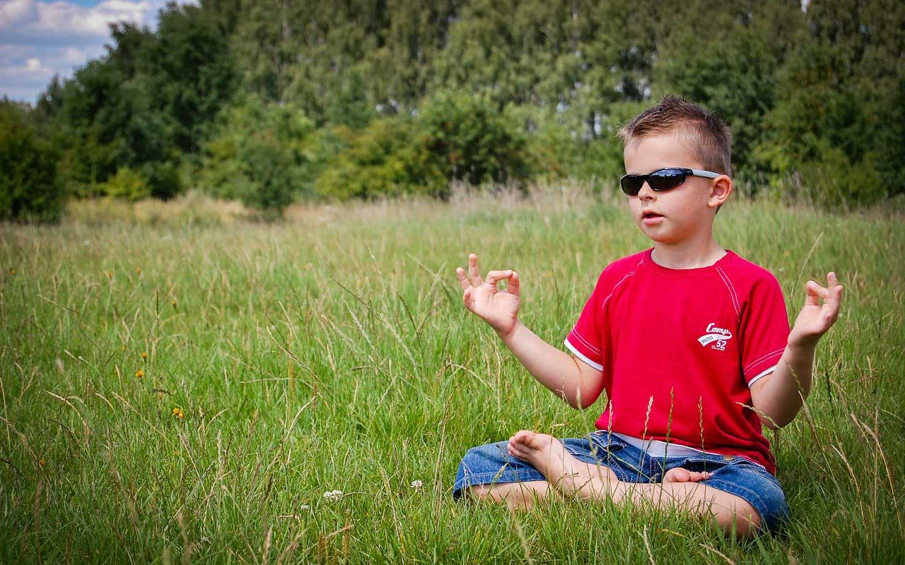 一个年轻男孩坐在与太阳镜的草，用他的手在凝思mudra（手势）。