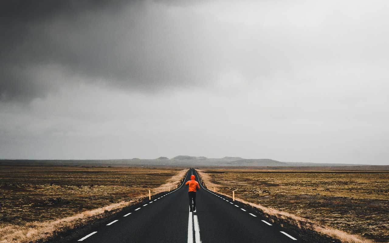 一个穿着橙色雨衣的人走在高速公路的中心线上，地平线上有风暴云。