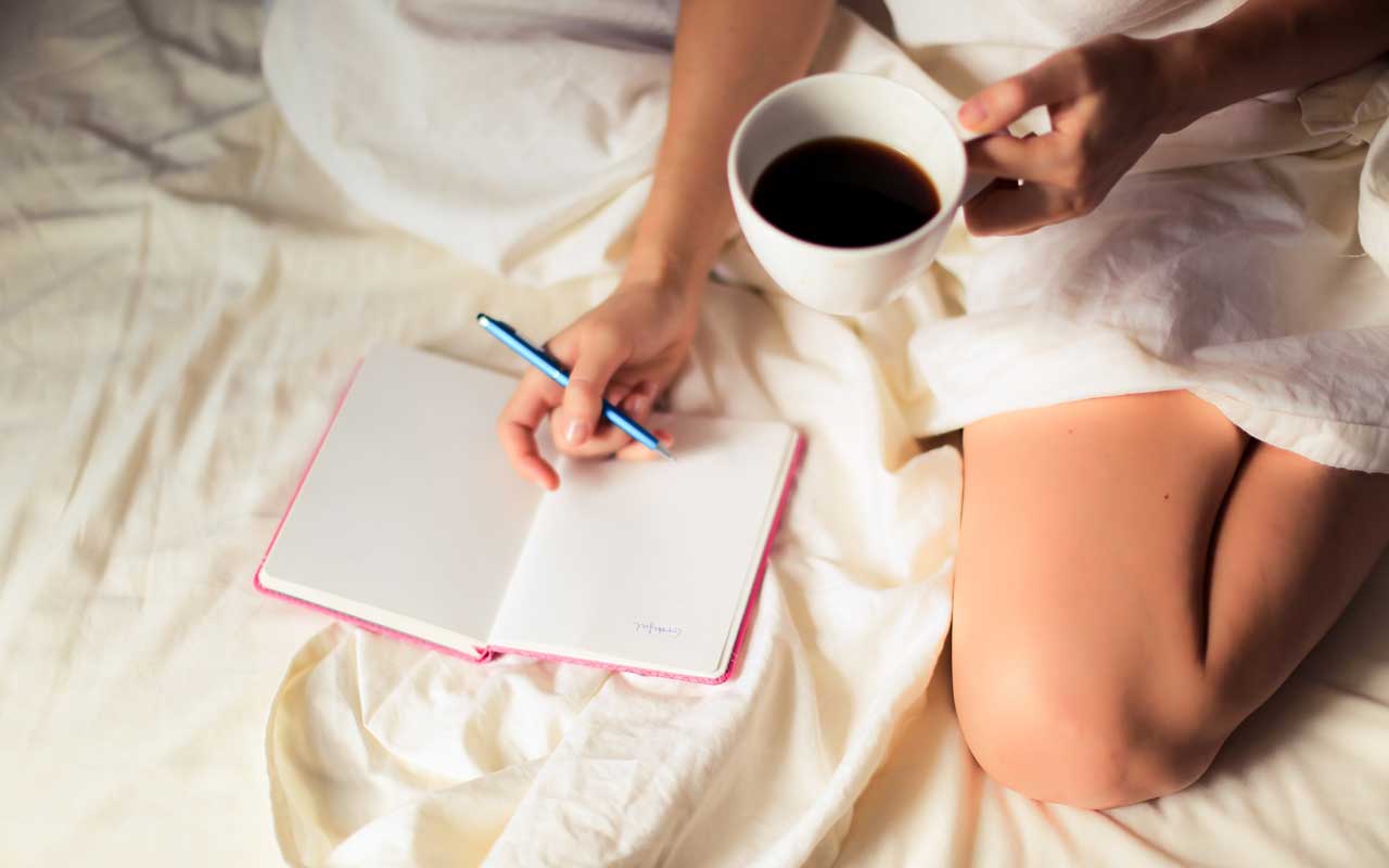 一个人用一杯咖啡在一只手床上在床上。