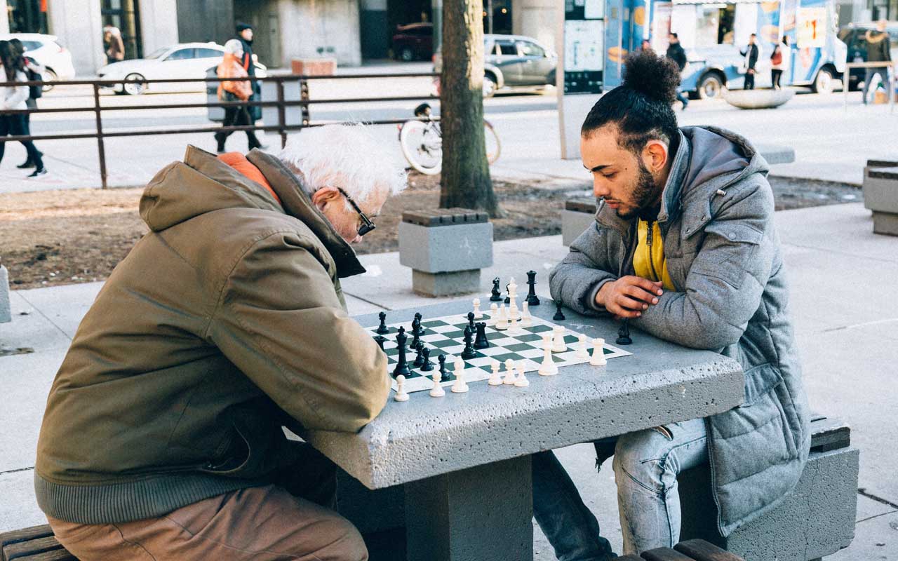 一个老人在公园里玩棋子有一个年轻的男人。国际象棋是成年人的一种认知活动，可能与您的年龄有益。