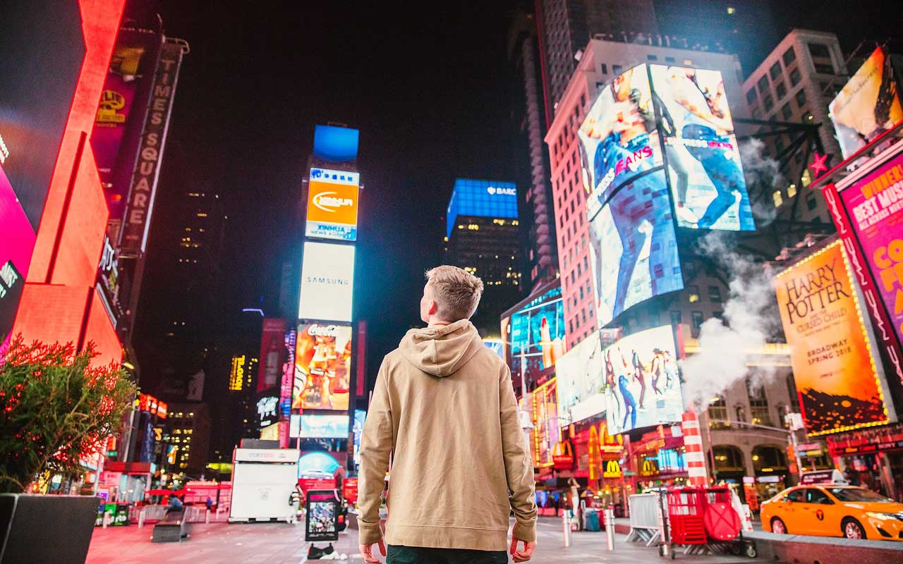 一个年轻人站在纽约市中心的时代广场，被广告包围。消除您的生活广告可以帮助您提高集中度。