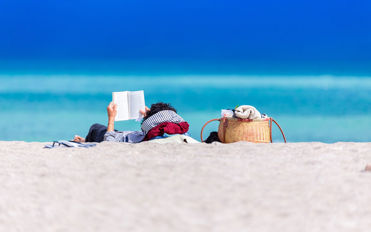 一个人拿着一本书在海滩上放松，可能会帮助他们在阅读时想象。