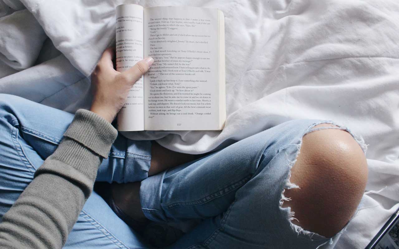 一个人坐在床上拿着一本书，同时使用视觉化阅读策略。
