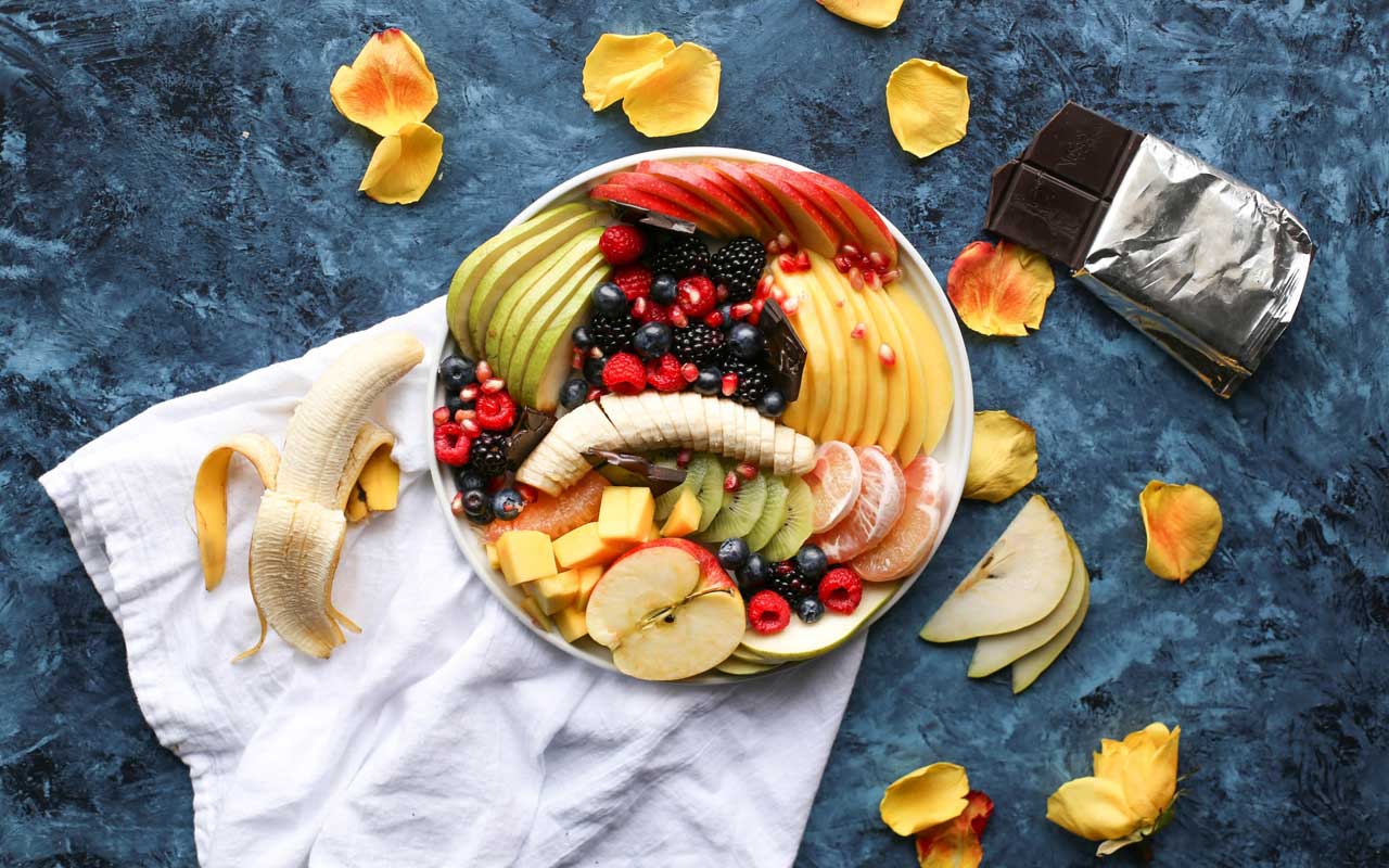 一块装满不同种类的水果，如香蕉，苹果，浆果和柑橘坐在黑巧克力的酒吧旁边。健康的食物可以提高记忆力。