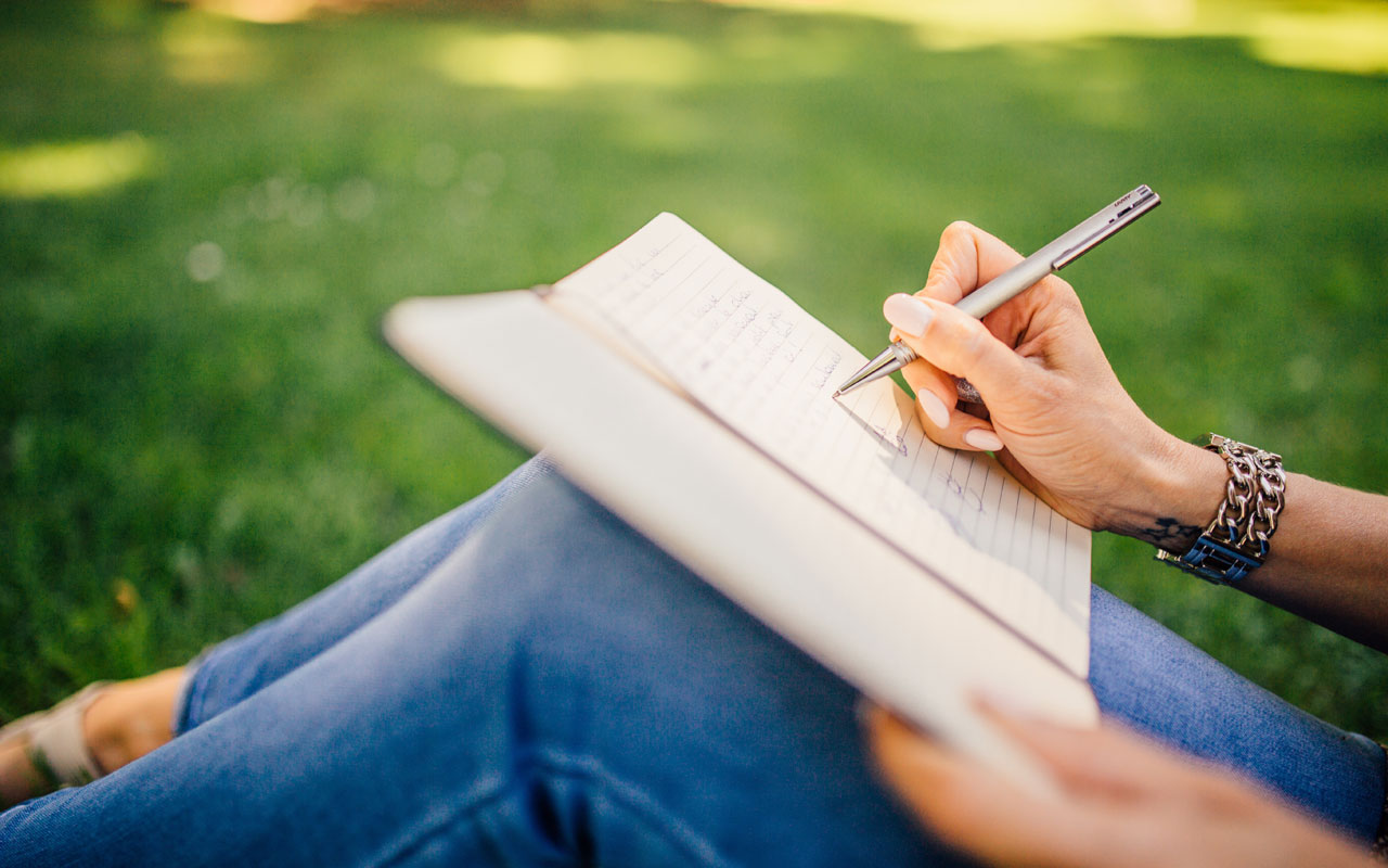 一个人坐在草地上写日记。写日记这样的练习可以帮助你集中注意力。