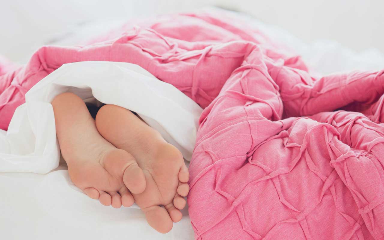 床上粉红色的被子下面伸出来一双脚。充足的睡眠是保持记忆力的关键。