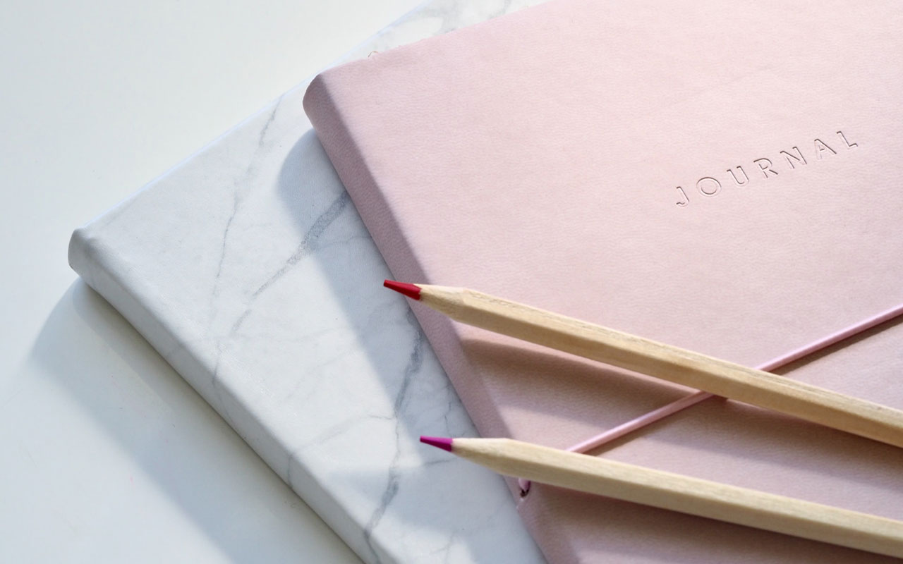 两本日记本靠在空白的表面上，上面有两支彩色铅笔。写日记可以帮助你学习如何有效地形象化。