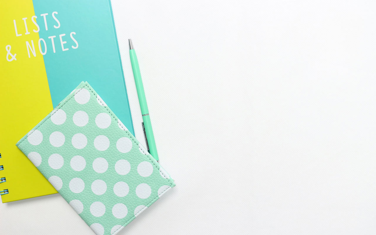 一本黄色和蓝色的笔记本，封面上写着“清单和笔记”，还有一本海泡沫绿色的日记本和一支笔。