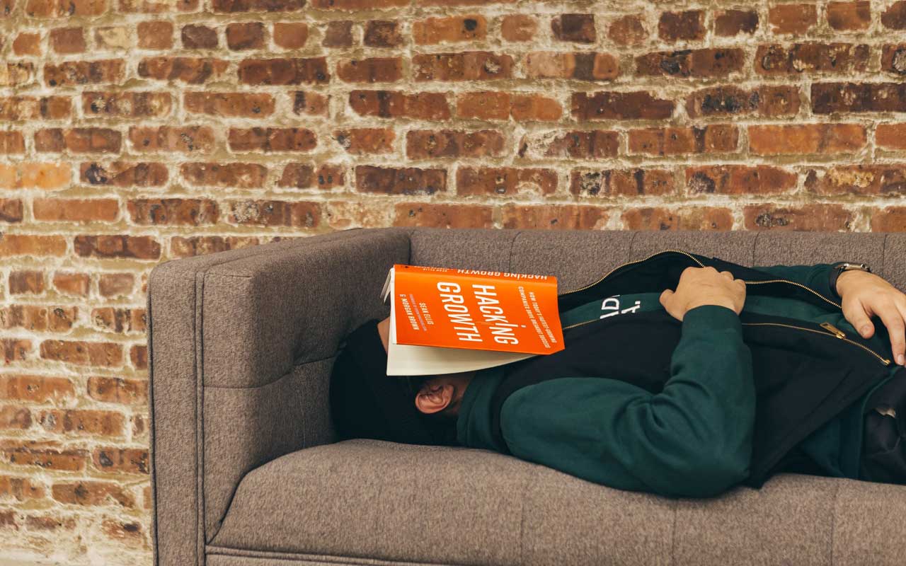 一个人在一个沙发上小睡一本书在他们的脸上。