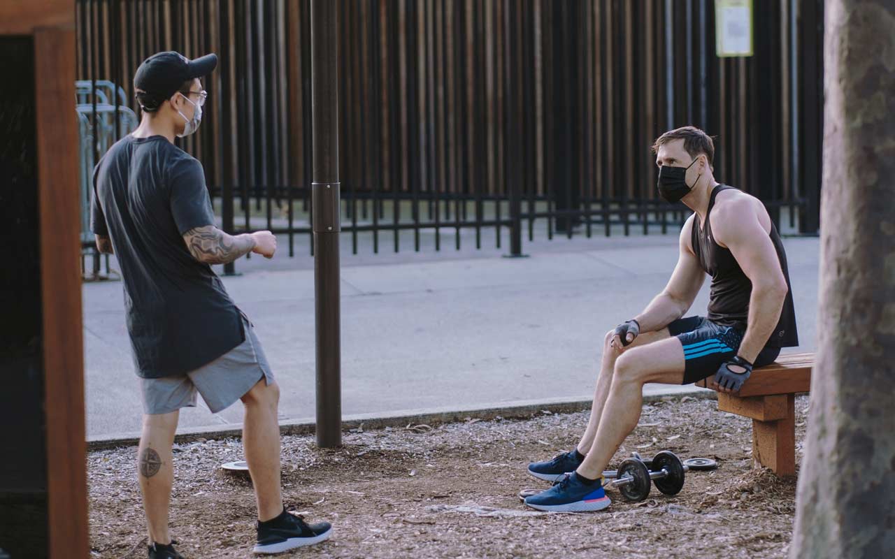 两个人戴着面具站在外面社交，一个人在锻炼。