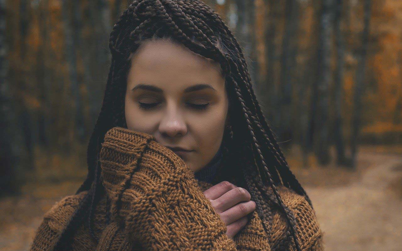有辫子的一个妇女在一个粗毛衣的森林道路站立有她的眼睛的闭合的毛线衣。