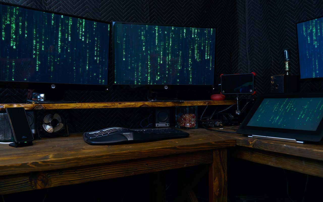 多台计算机屏幕坐在桌子上，运行代码，看起来像电影中使用的类型。