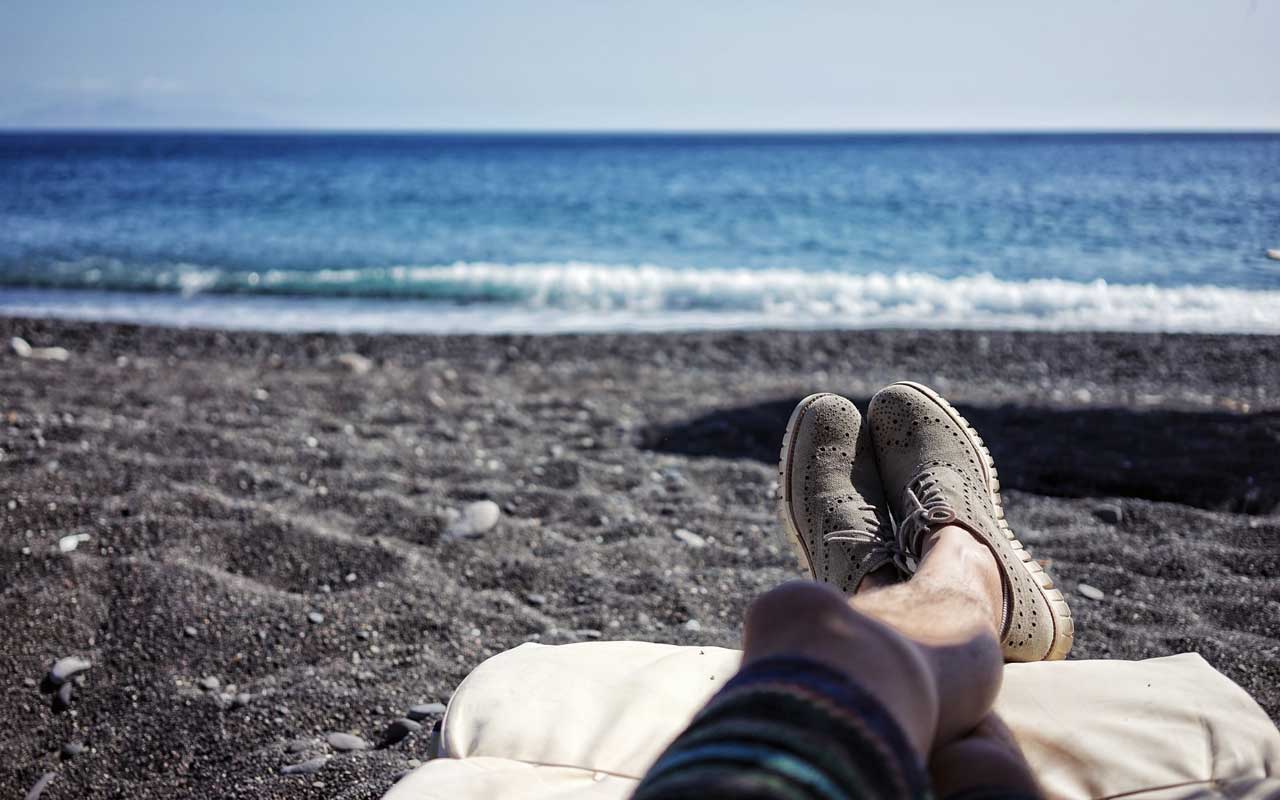 一个人在一个黑沙滩上放松，鞋子和腿上。