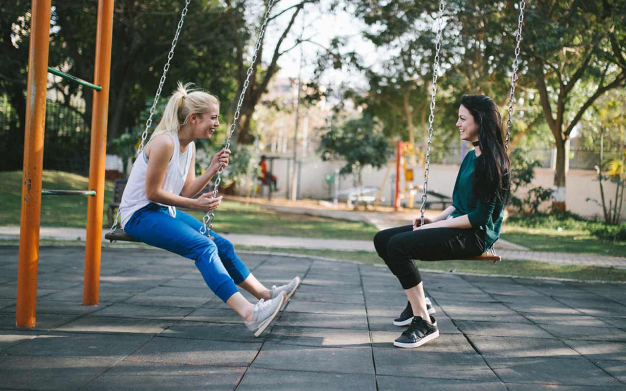 两个女人坐在摇摆外面在公园。说话是快速学习西班牙语的最佳方式之一。